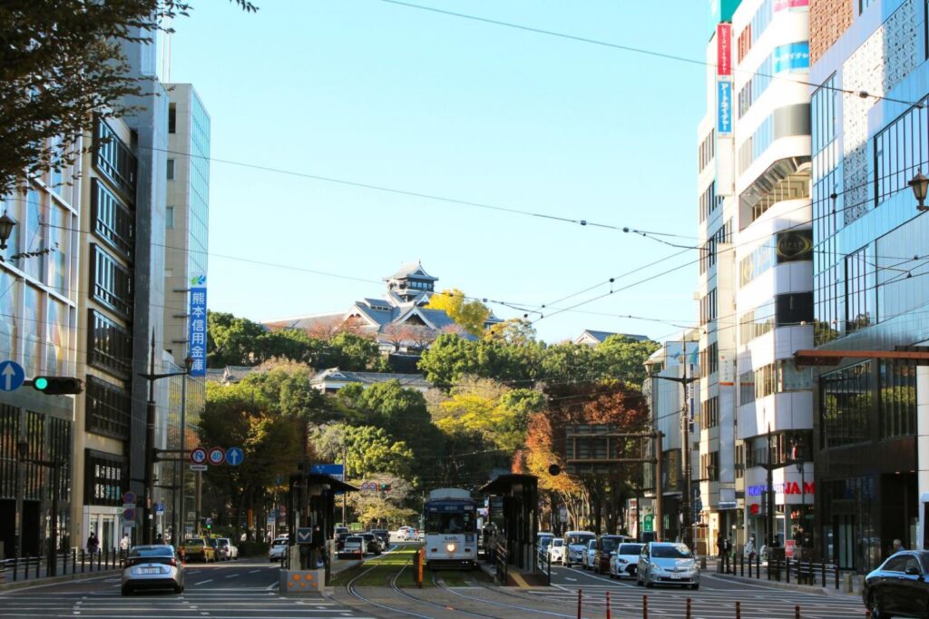 A tram on a street in central Kumamoto City with the castle behind
