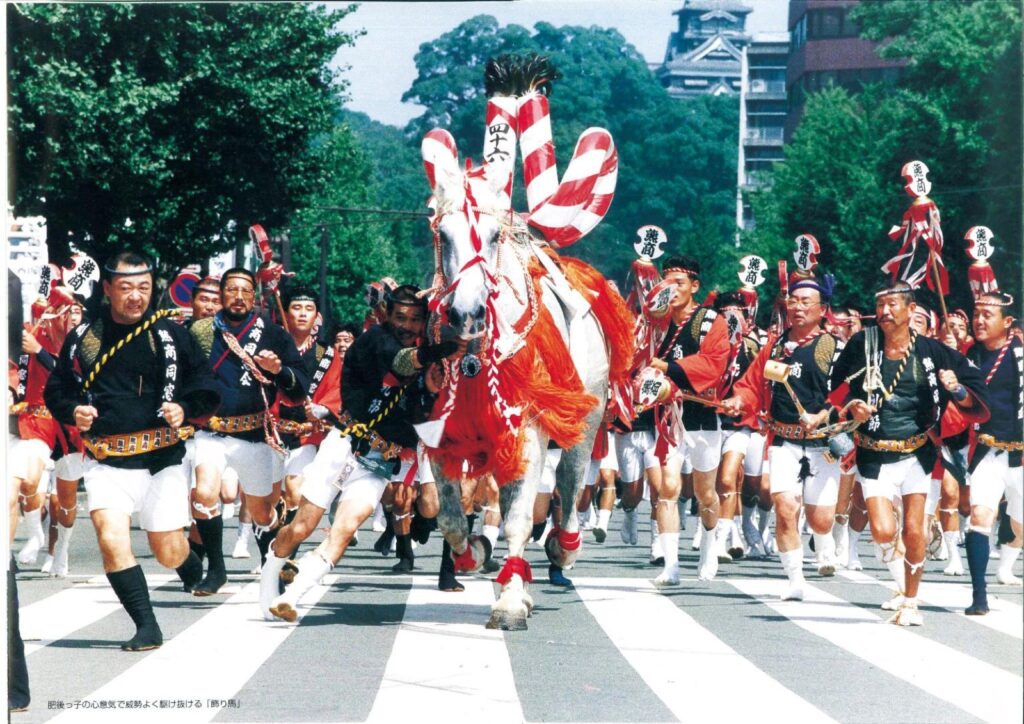 Decorated horses and people in festival clothes in a street parade, with Kumamoto Castle behind